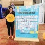 Emma Miner Emma Miner, 2023 BCPI Summer Scholar, standing beside a large display board titled Adopta à Una Problema, featuring numerous sticky notes.