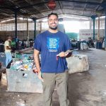 Mustafa Ahmad A person in a blue T-shirt stands smiling in a large industrial recycling facility.