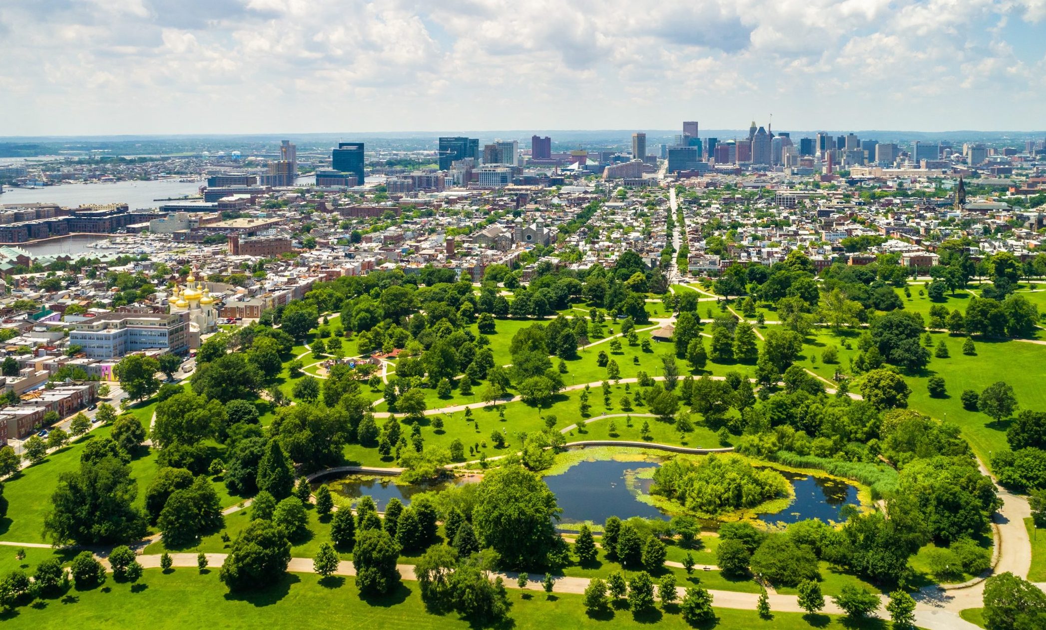 Baltimore, Maryland Aerial view of Baltimore with an expansive green park, surrounded by a dense urban skyline under a sunny sky with scattered clouds.
